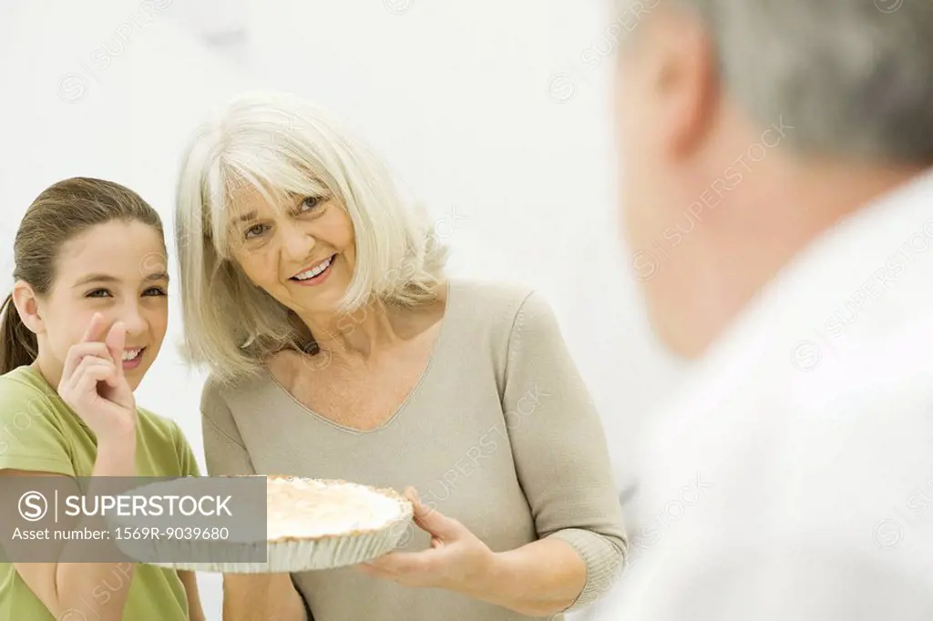 Grandmother and granddaughter offering pie to man in foreground, smiling
