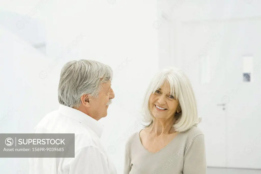 Senior couple standing face to face, woman smiling at camera