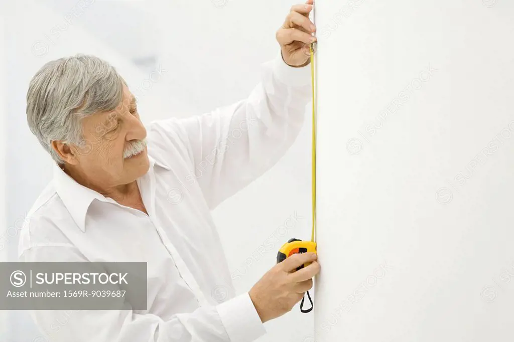 Senior man using measuring tape on wall