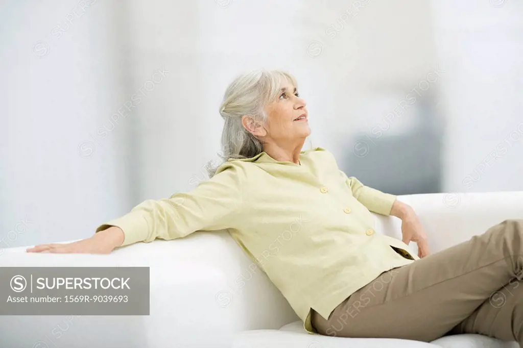 Senior woman sitting on couch, looking up, smiling