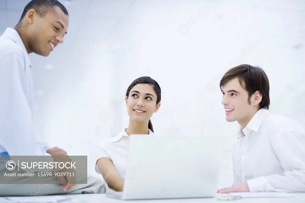 Young professionals sitting around laptop computer, smiling