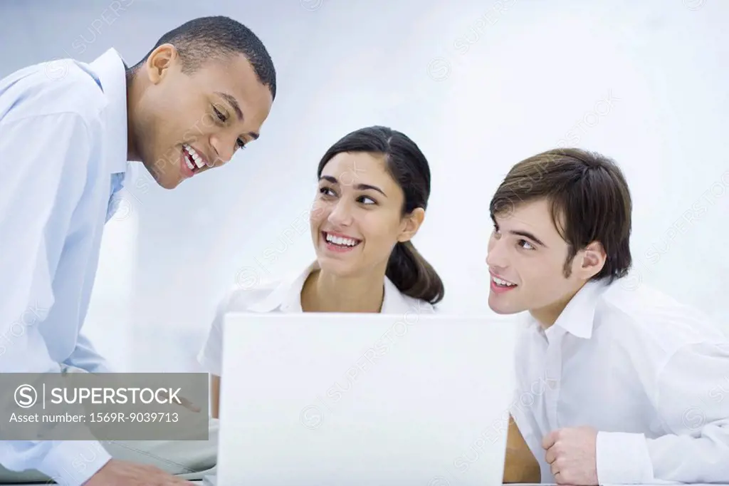 Young professionals sitting around laptop computer, leaning close together, smiling