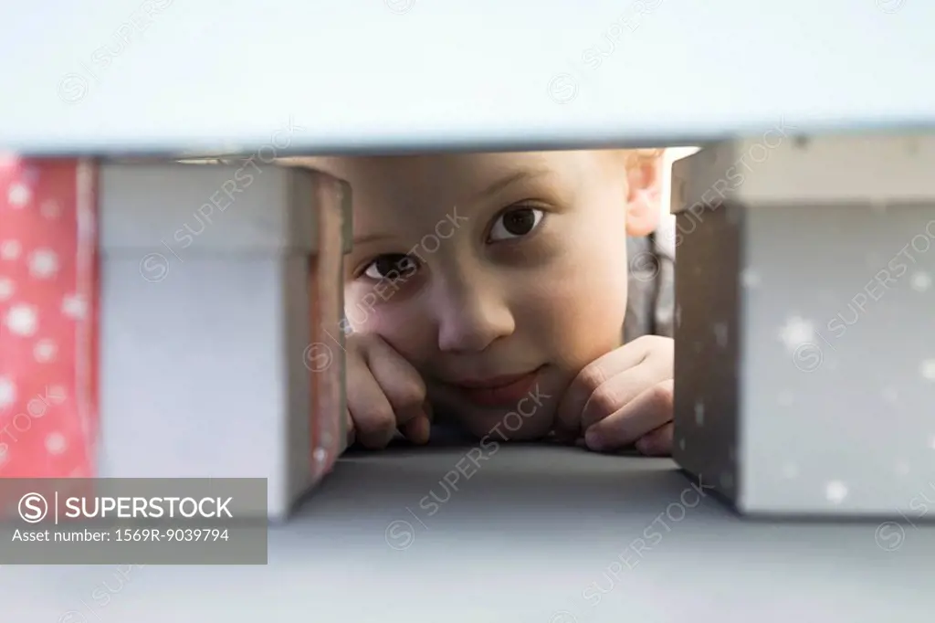 Little boy hiding behind pile of presents, peeking at camera
