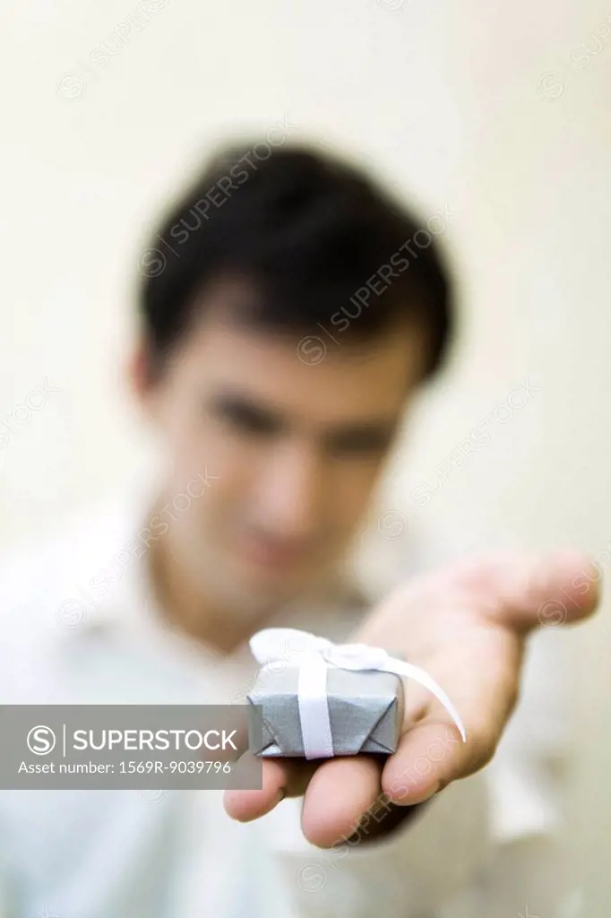 Man holding out small gift box, focus on foreground