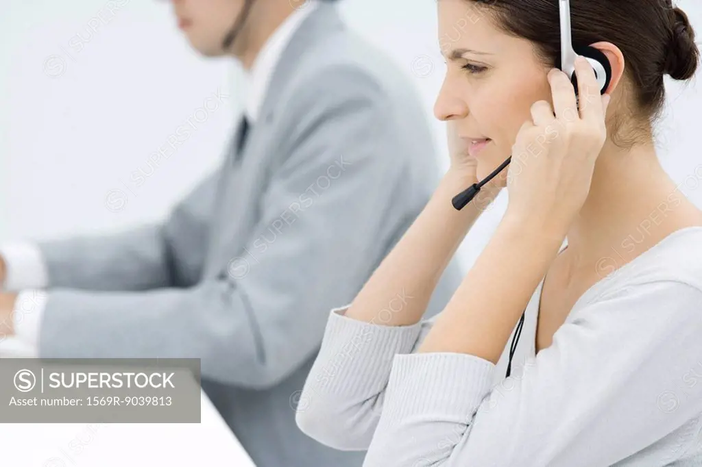 Professional woman adjusting headset, male colleague in background, side view