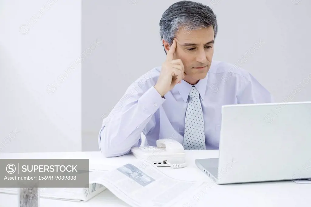 Businessman sitting at desk, looking at laptop computer, holding head