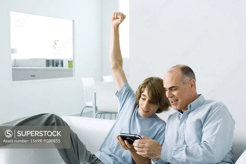 Teen boy showing handheld video game to father, arm raised