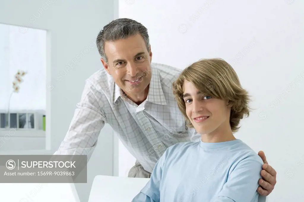 Father and son smiling at camera, man´s arm around teenager´s shoulder