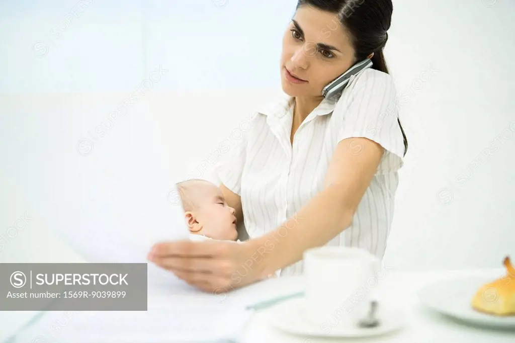 Professional woman using cell phone, holding baby, reviewing document