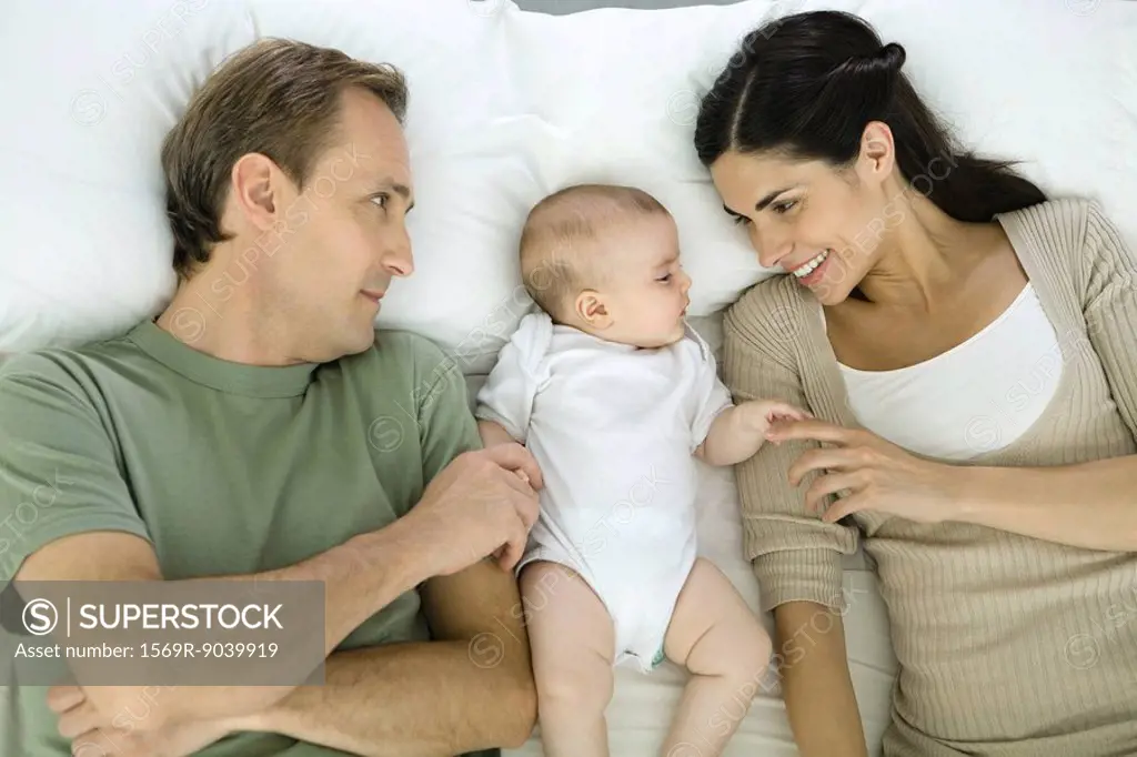 Family resting on bed, baby lying in between parents, overhead view