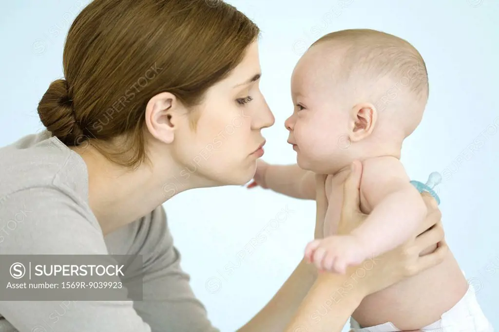 Mother holding baby up close to face, both smiling at each other