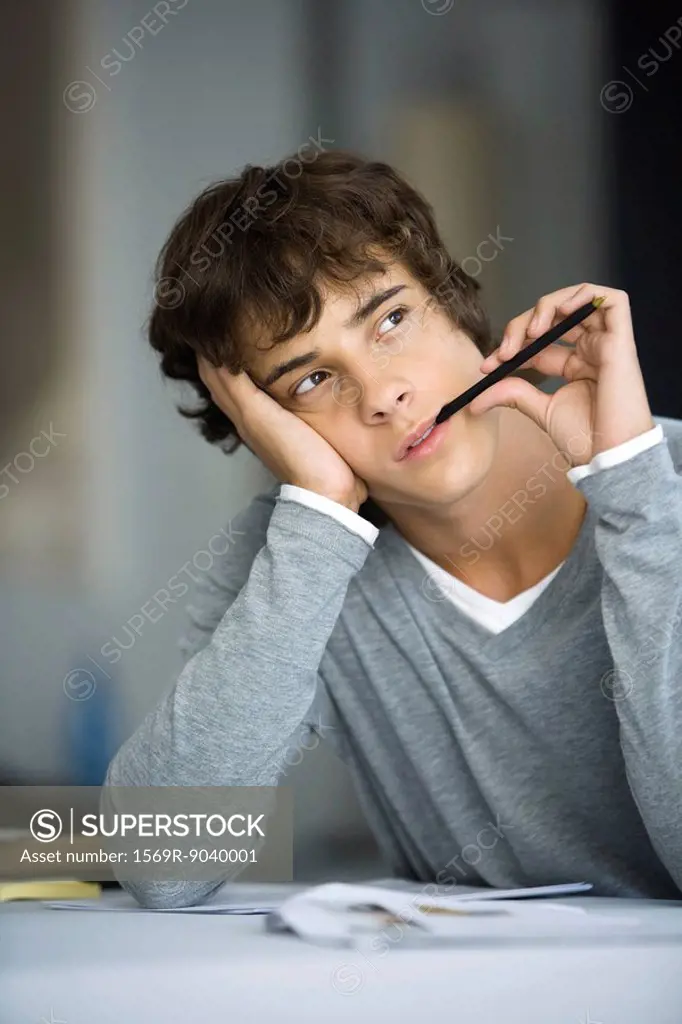 Young man with pen in mouth looking away, daydreaming