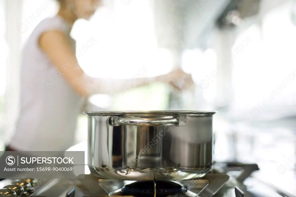 Pot cooking on stove, woman in background