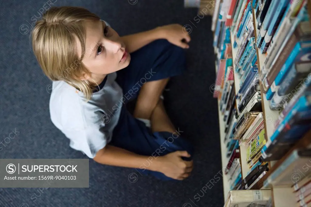 Boy sitting on floor looking up at shelves full of books