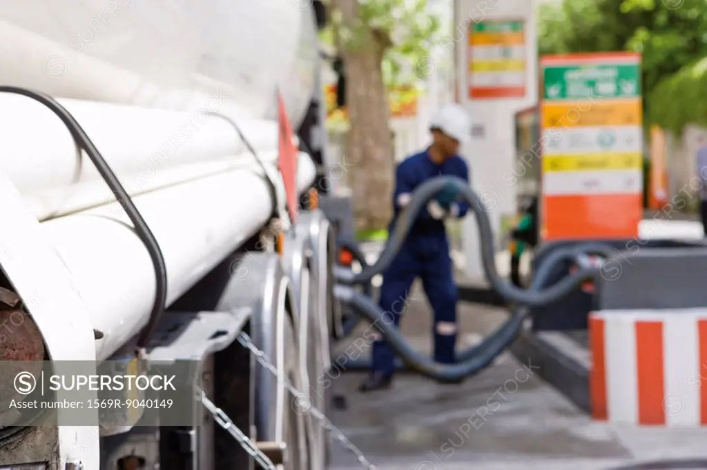 Hoses connected to fuel tanker outlets transferring fuel to gas station storage tanks