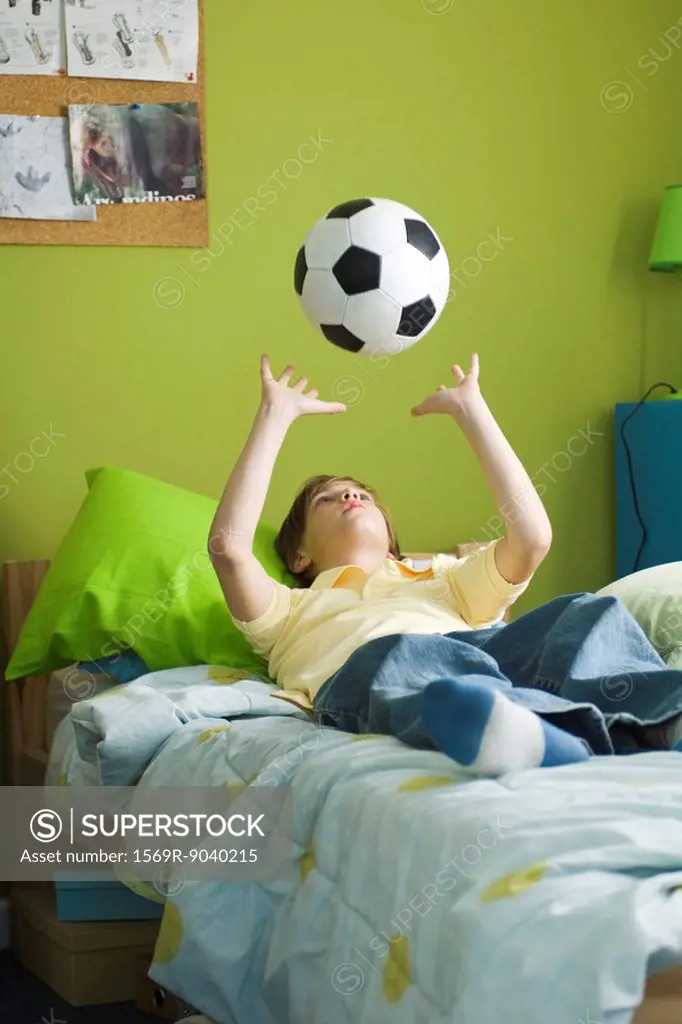Boy lying on bed idly tossing ball into air