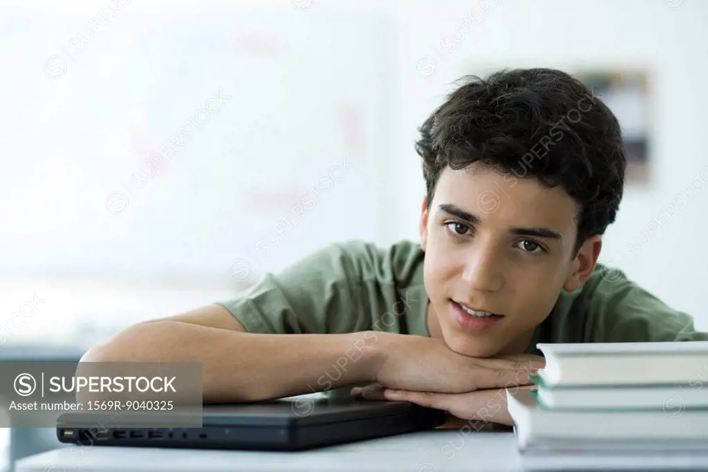 Male high school student sitting at desk with head resting on arms, portrait