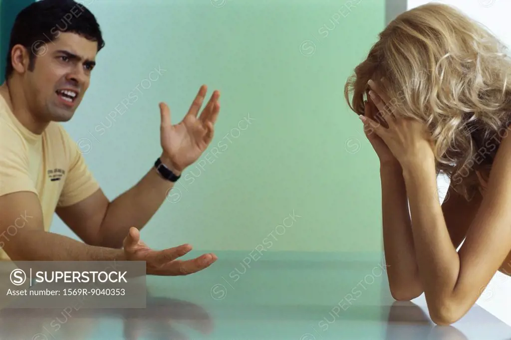 Couple arguing at table, woman holding head