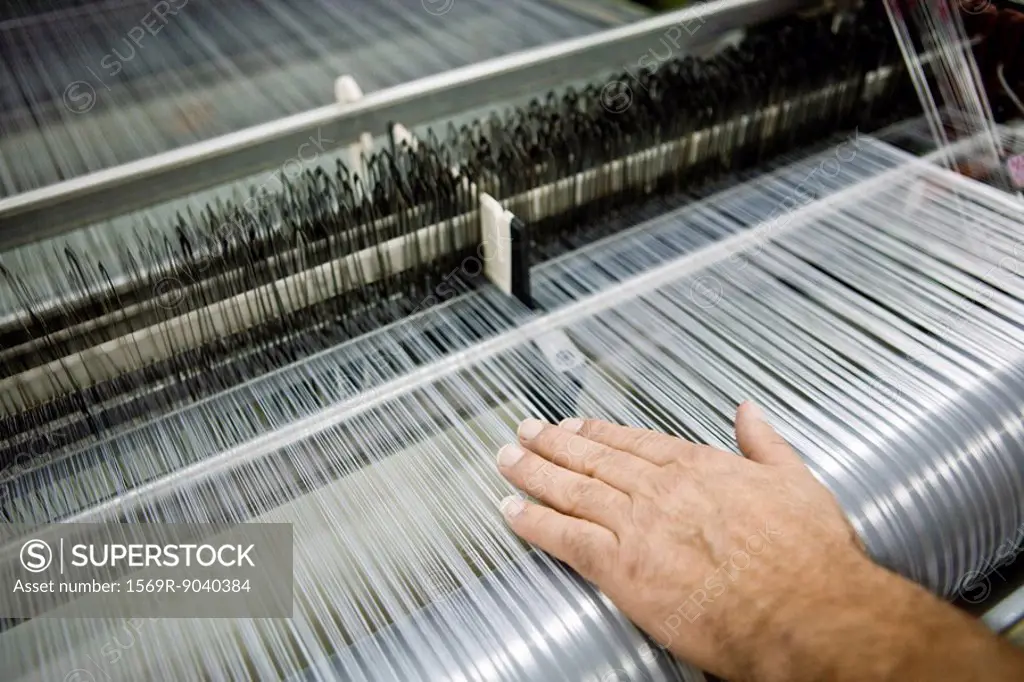 Weaving mill, machinist manually checking thread tension on a loom