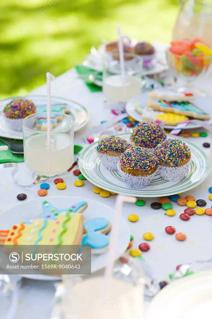 Iced cookies and cupcakes on table decorated with streamers and candy