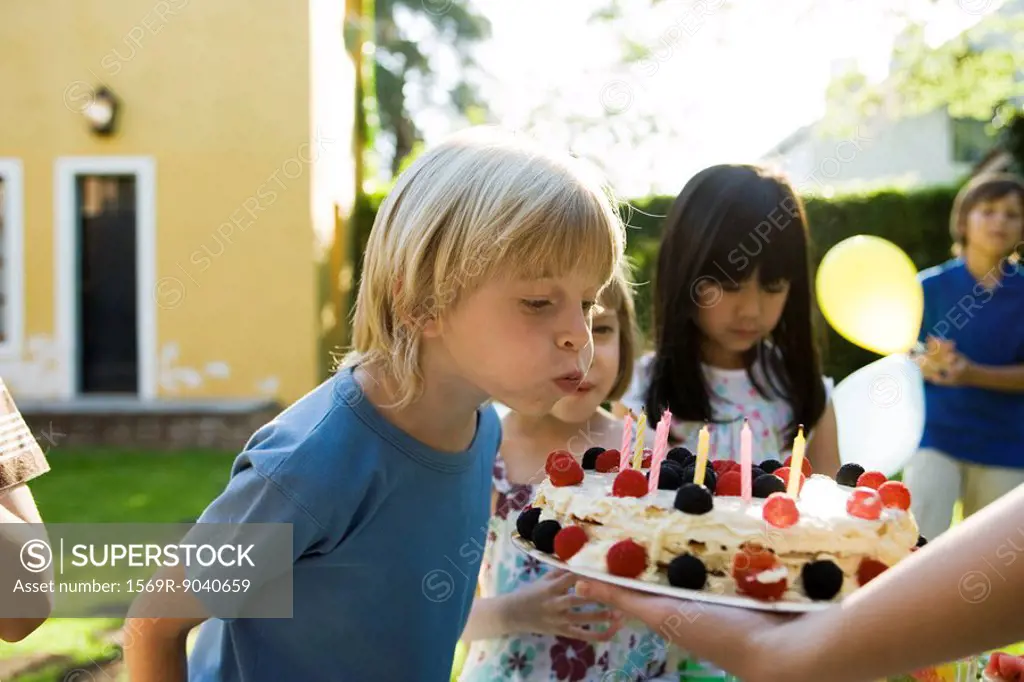 Boy blowing out candles on birthday cake at outdoor birthday party