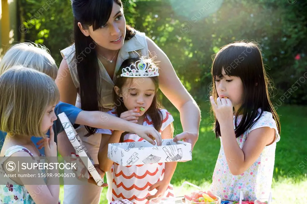Mother helping daughter open gift at birthday party