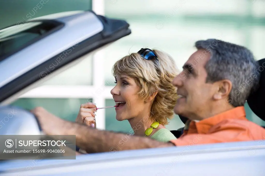 Mature couple in car together, woman putting on lip gloss