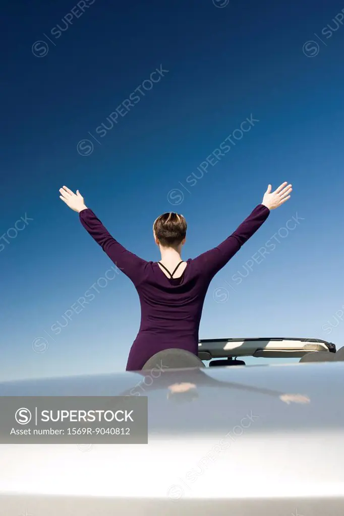 Woman with arms raised standing in parked convertible enjoying the outdoors