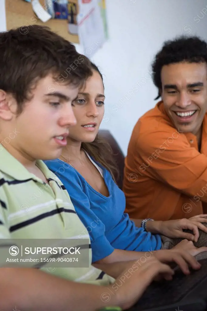 Male college student using laptop computer, classmates sitting alongside watching