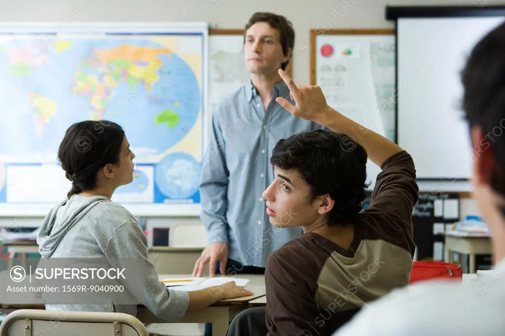 High school student raising hand in class, looking over shoulder