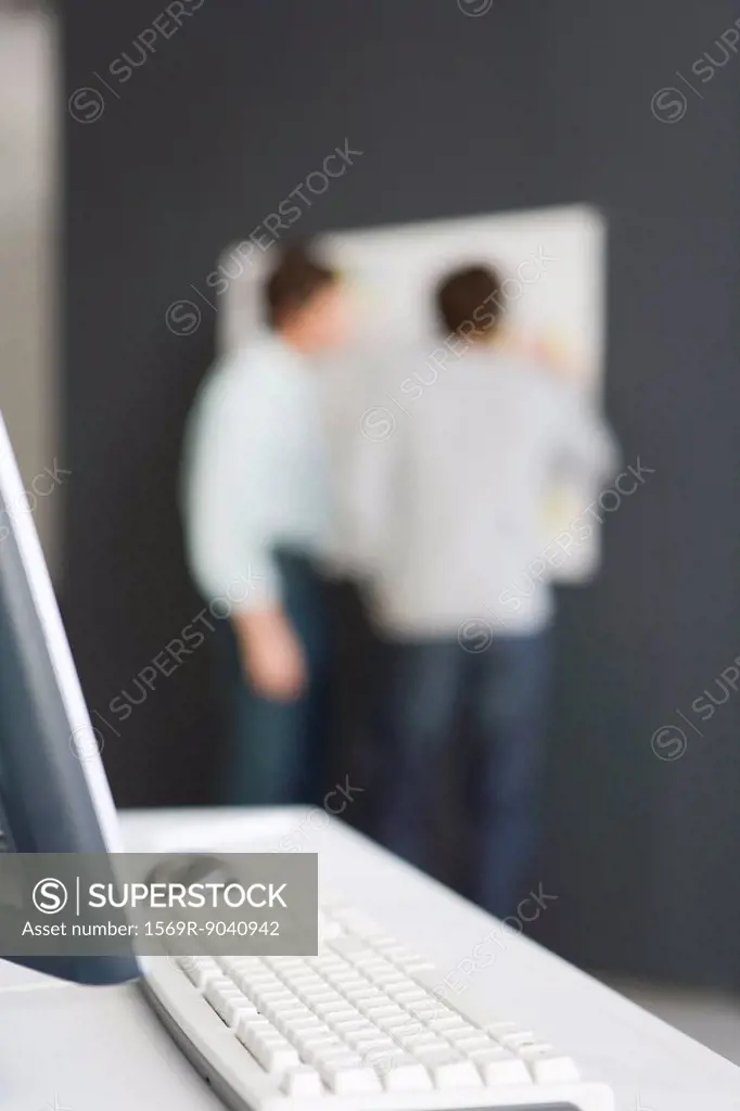 Desktop computer and keyboard, unrecognizable men in background