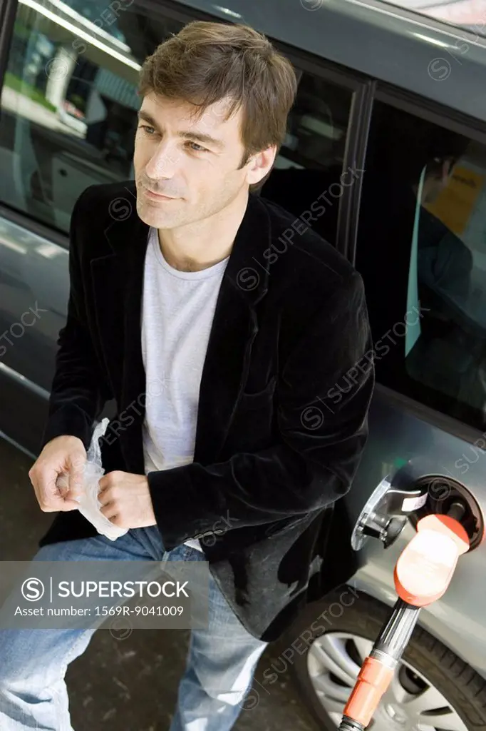 Man at gas station leaning against car waiting for gas tank to fill
