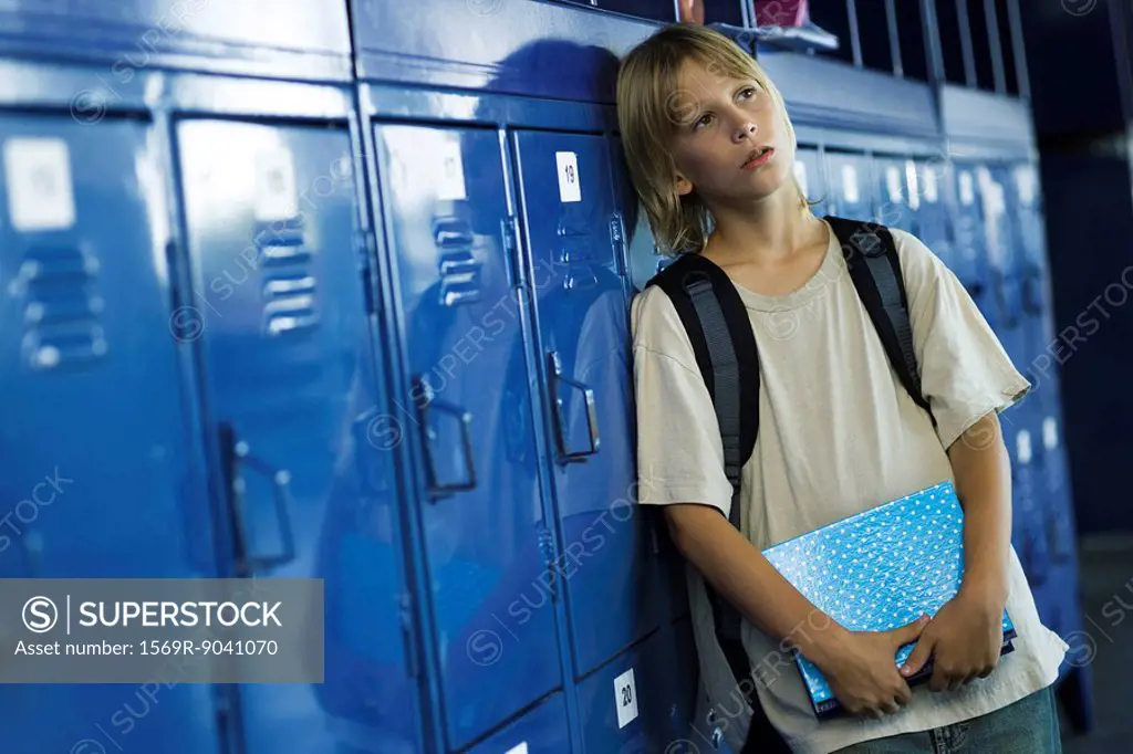 Male junior high student leaning against lockers looking away