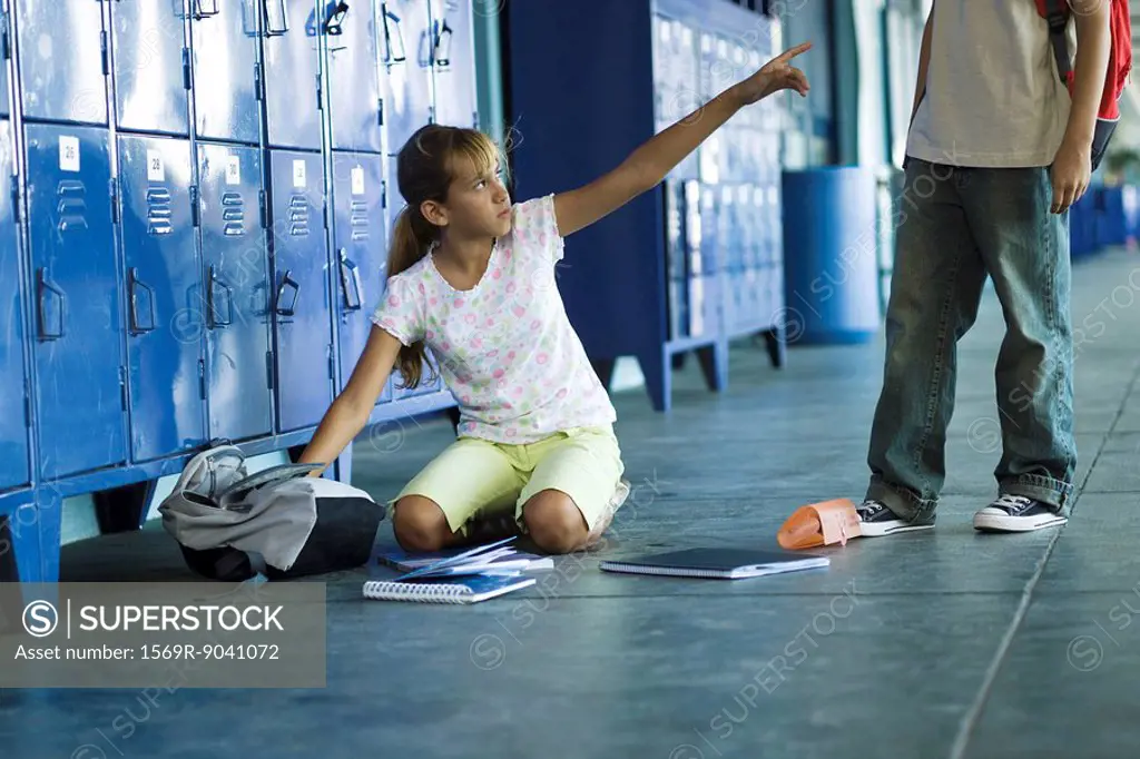 Female junior high student sitting on floor pointing angrily up at boy standing over her