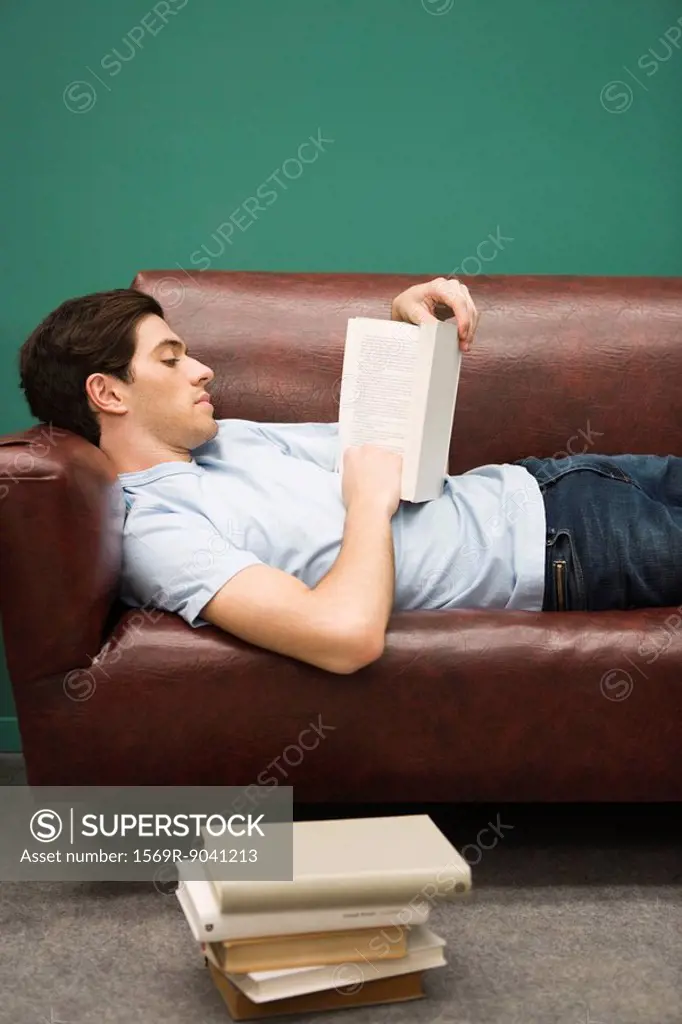 Young man relaxing on sofa with book