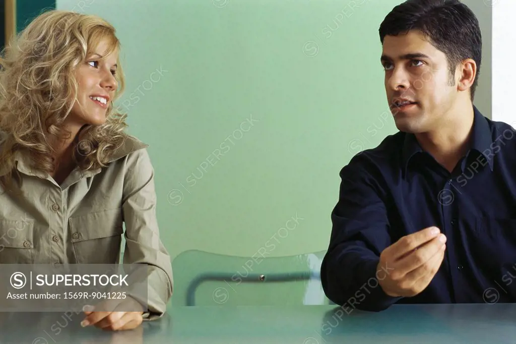 Man and woman sitting at table with empty chair between them, having conversation