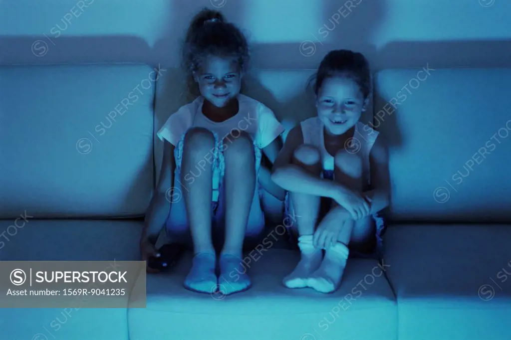 Two girls watching TV together at night, both smiling
