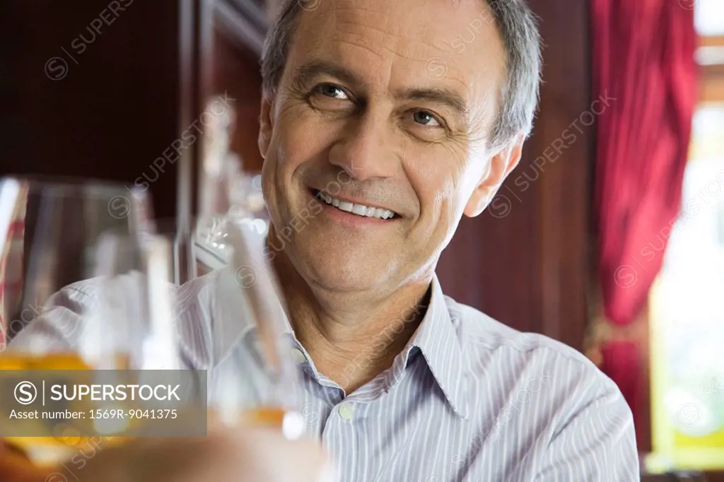 Mature man clinking glasses with companion in restaurant