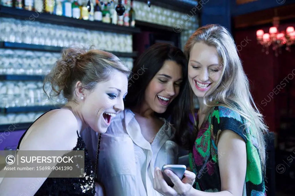 Friends together at bar, woman showing cell phone to others