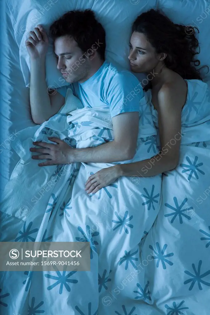 Couple together in bed, woman embracing man, watching him sleep