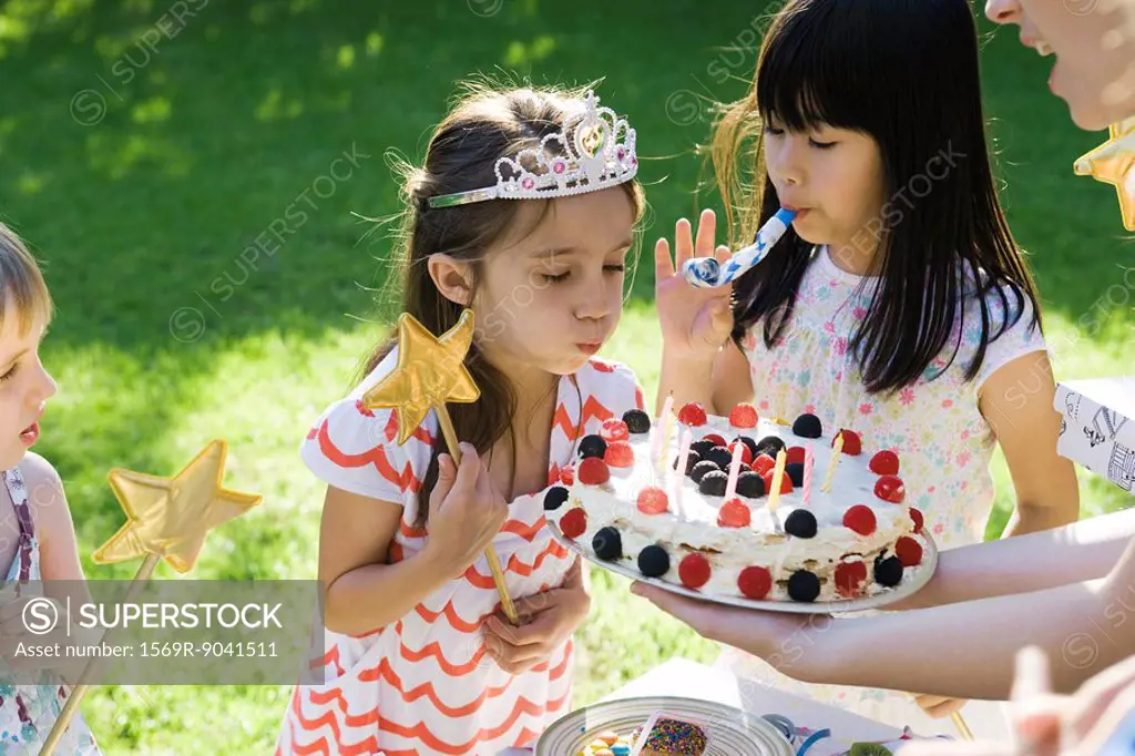 Girl blowing out candles on birthday cake at outdoor birthday party