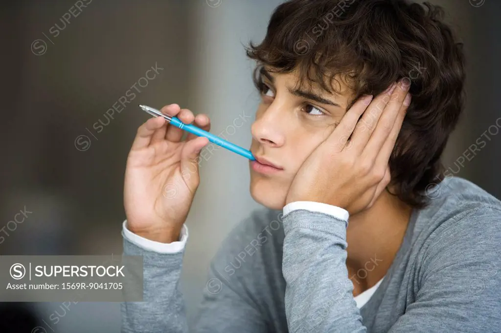 Young man daydreaming, absently holding pen in mouth