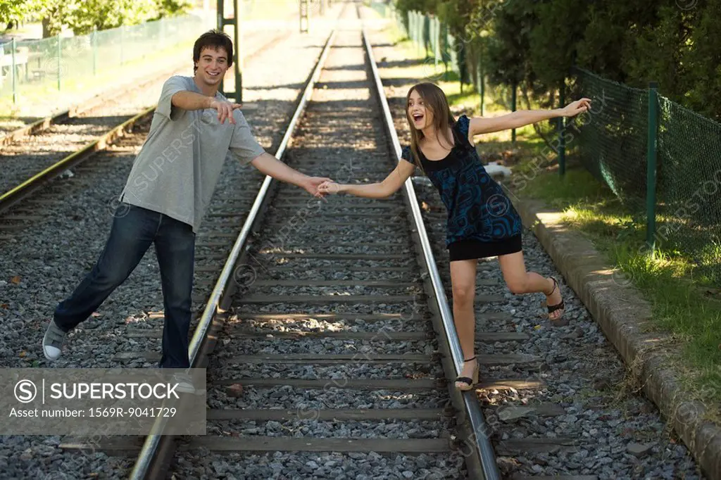 Young couple walking on rail track, holding hands