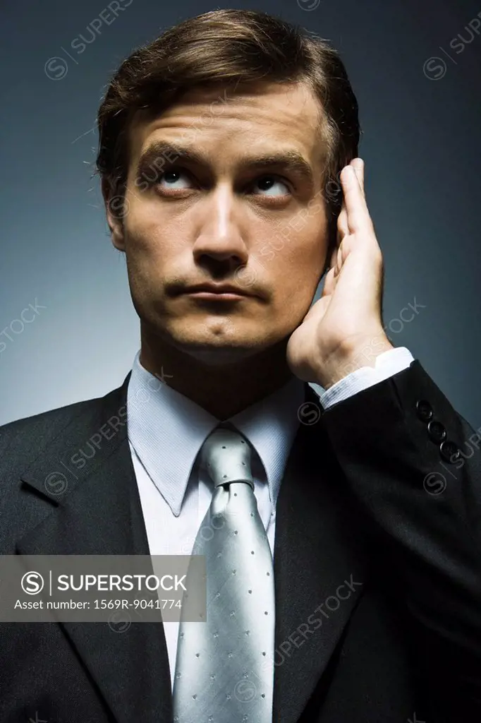 Businessman with hand cupped around ear listening attentively