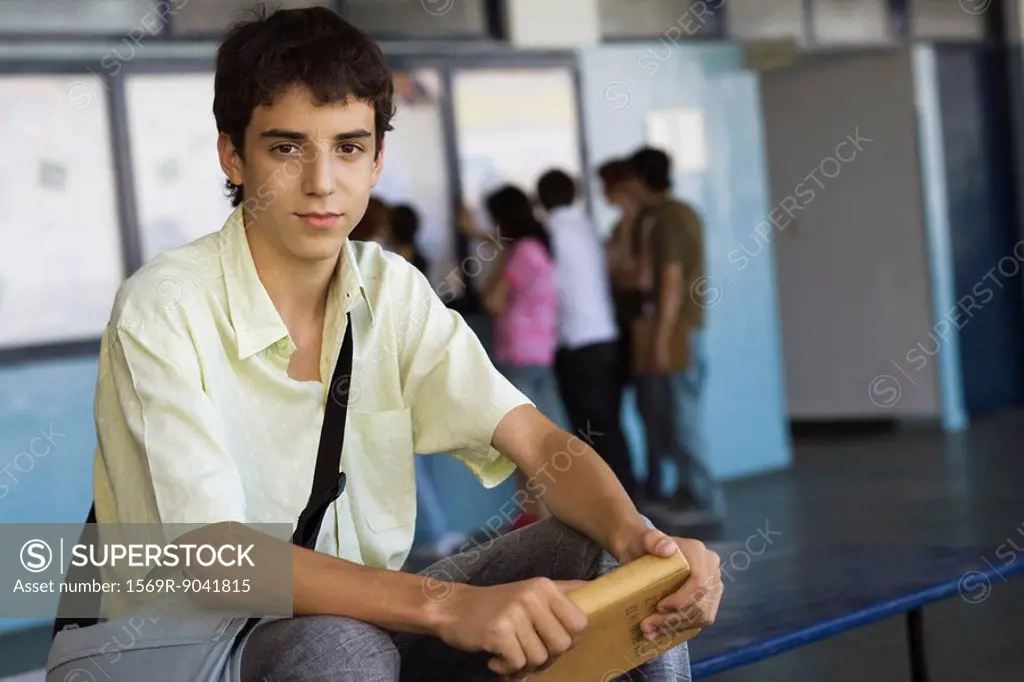 Male high school student sitting on bench holding hardback book