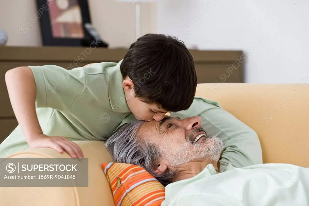 Young boy kissing napping grandfather on forehead