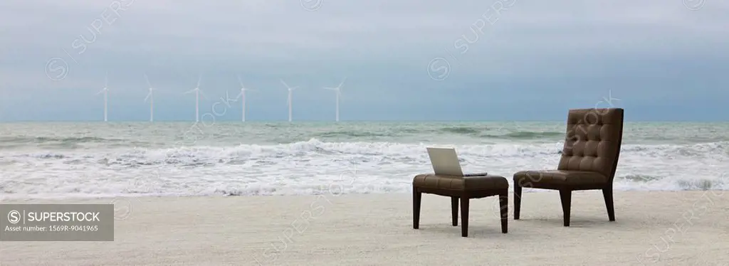 Chair and laptop computer on beach, wind turbines visible in distance