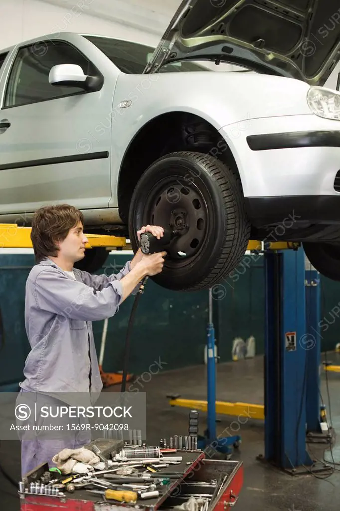 Mechanic changing tires of car elevated on hydraulic lift