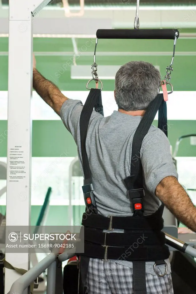Man exercising with assistance of rehabilitation harness supporting body weight