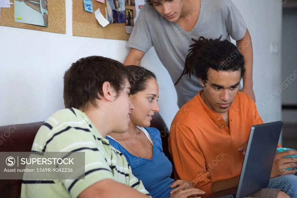 College students gathered around classmate using laptop computer